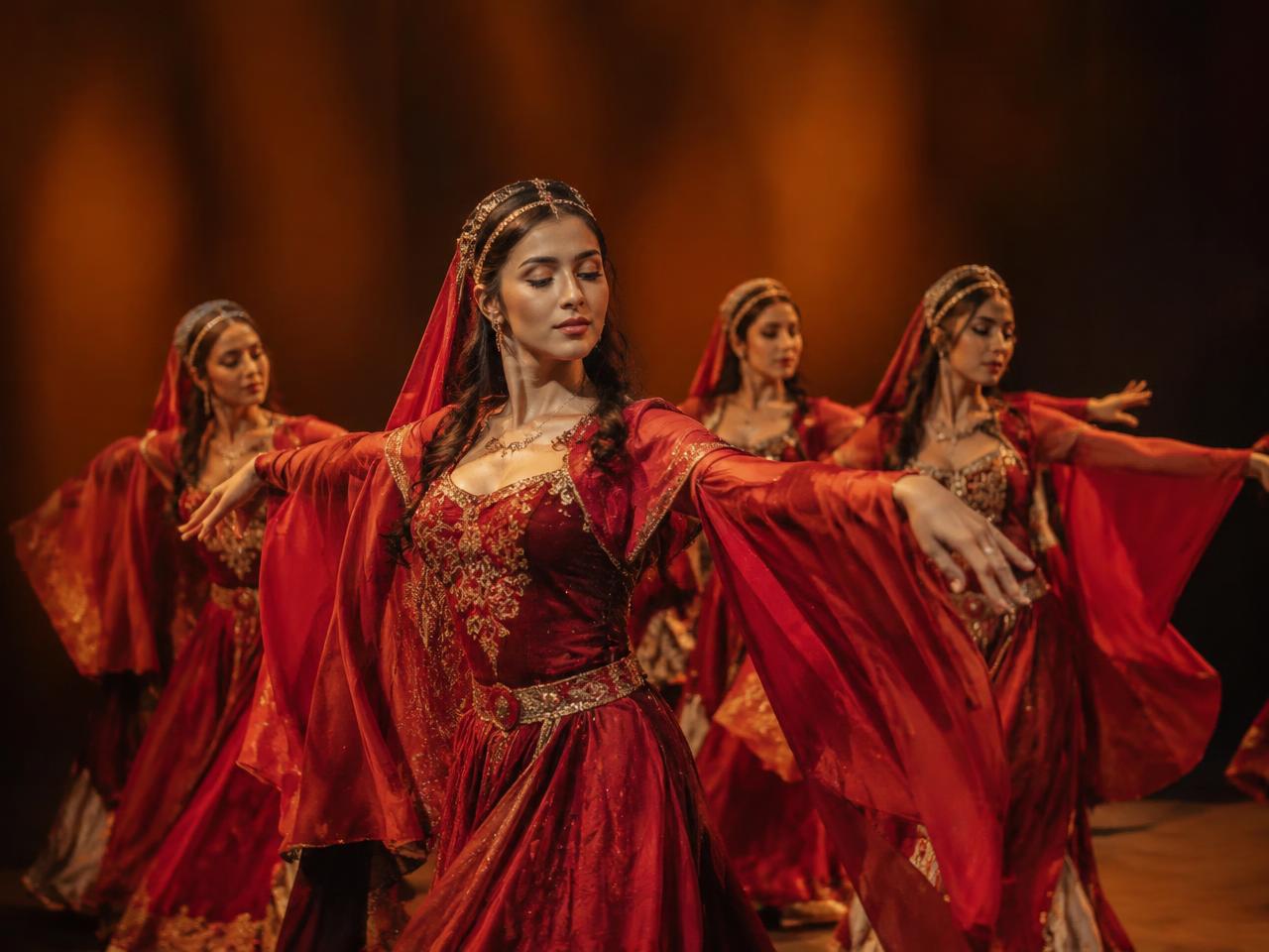 Dancers in crimson and gold Persian costumes performing on a warm-lit stage