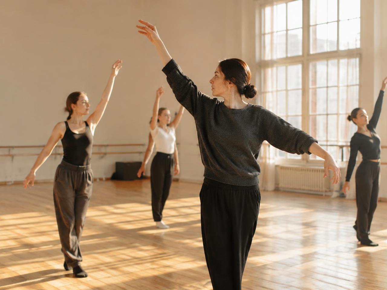 Choreographer marking movement with dancers in a sunlit studio
